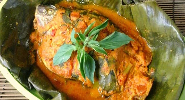 Ikan berbumbu tempoyak oranye dengan daun kemangi di atas daun pisang