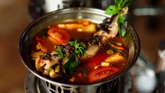 Pindang ikan berkuah merah dengan tomat, nanas, cabai, dan daun kemangi di dalam panci
